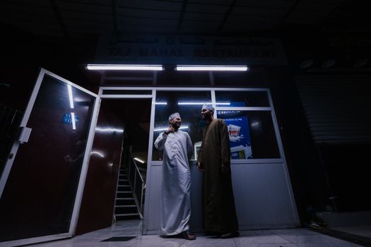 Two men share a moment outside Taj Mahal Restaurant in Muscat, Oman at night.