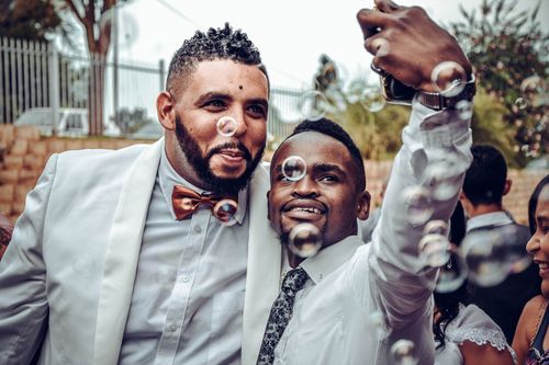 Free Two men taking a selfie at a wedding, surrounded by bubbles, celebrating joyfully. Stock Photo