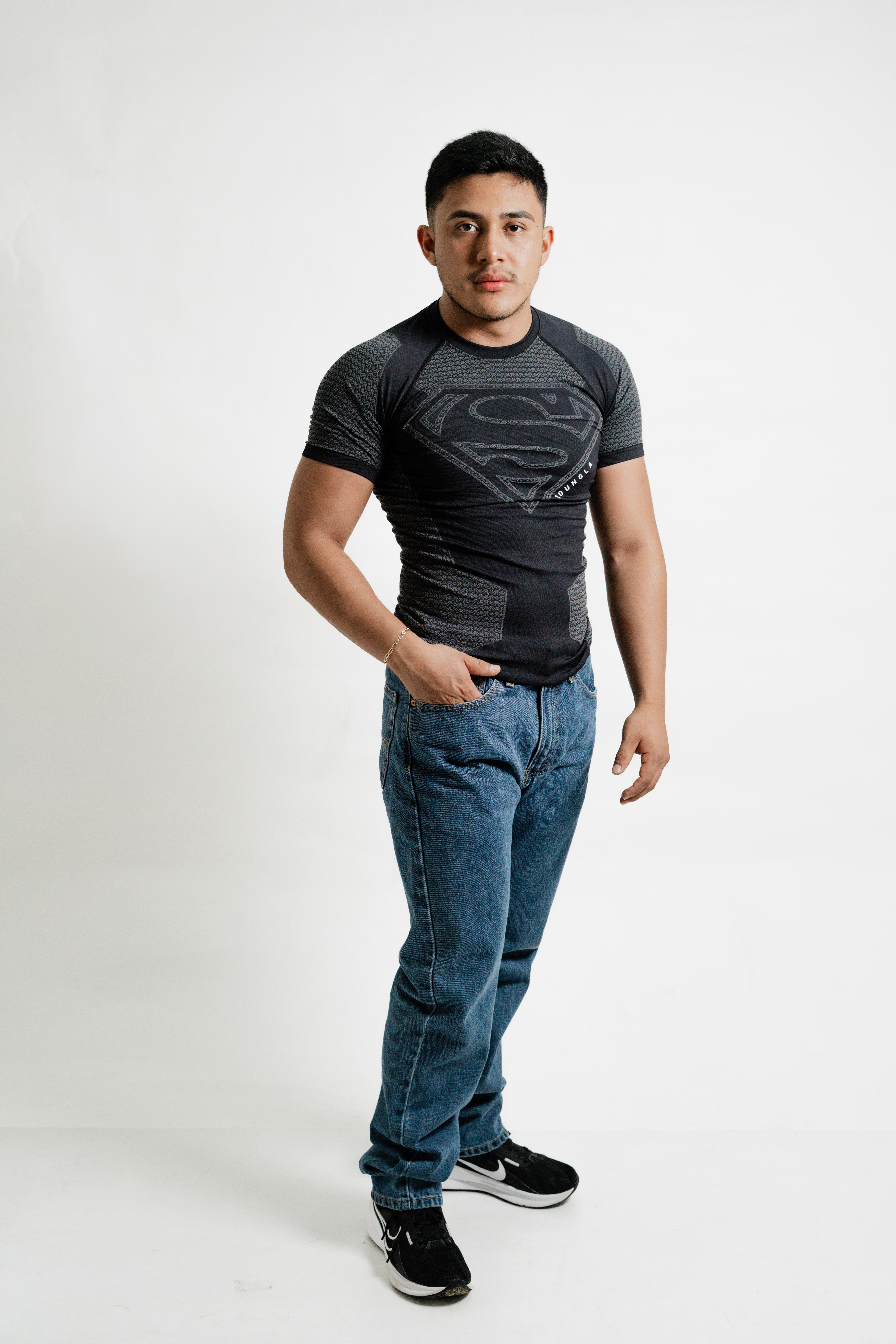 Portrait of a young man wearing a superhero t-shirt, standing in a studio setting.