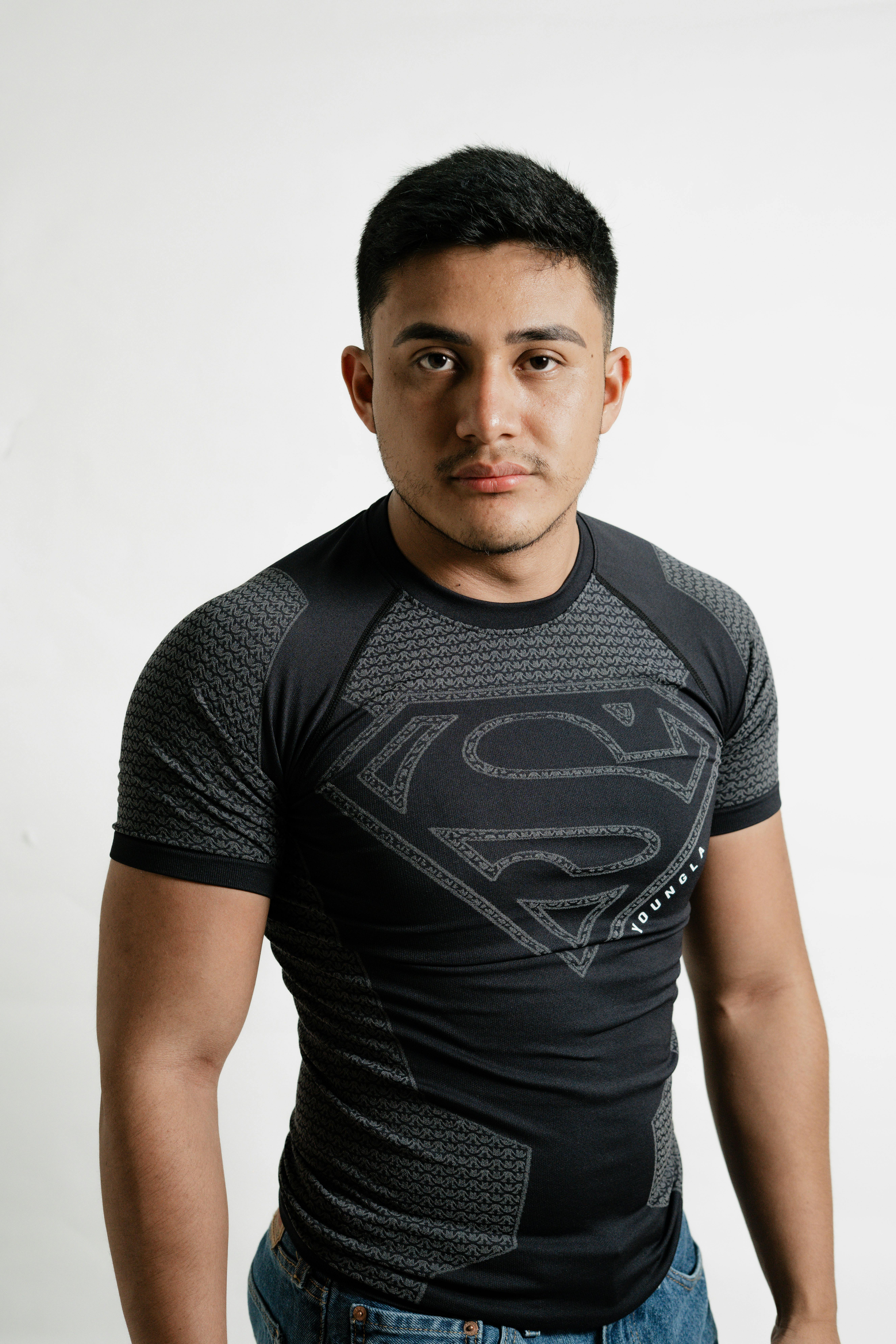 Portrait of a young man standing confidently in a black Superman shirt on a white background.