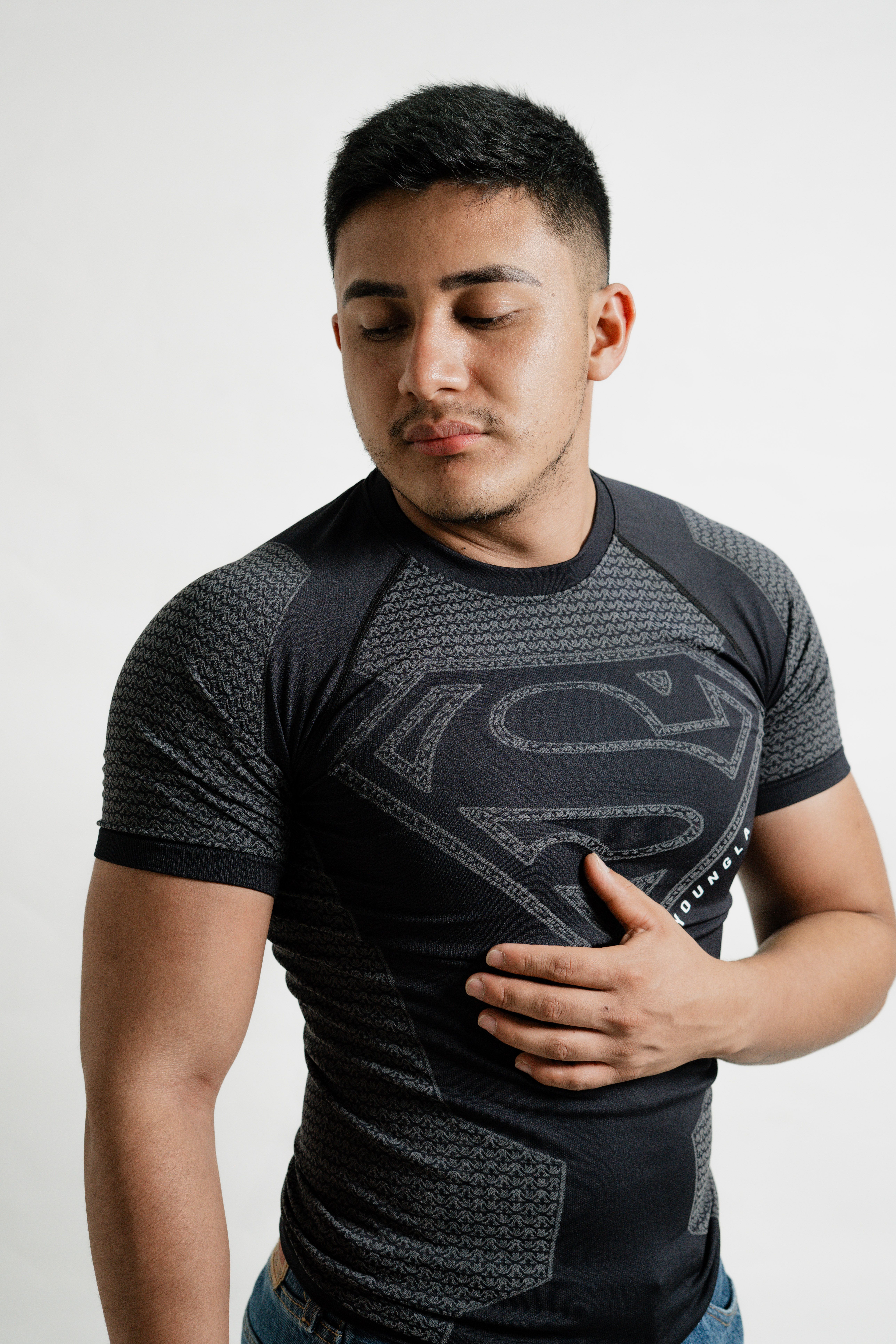 Portrait of a young man posing confidently in a superhero-themed shirt against a plain background.