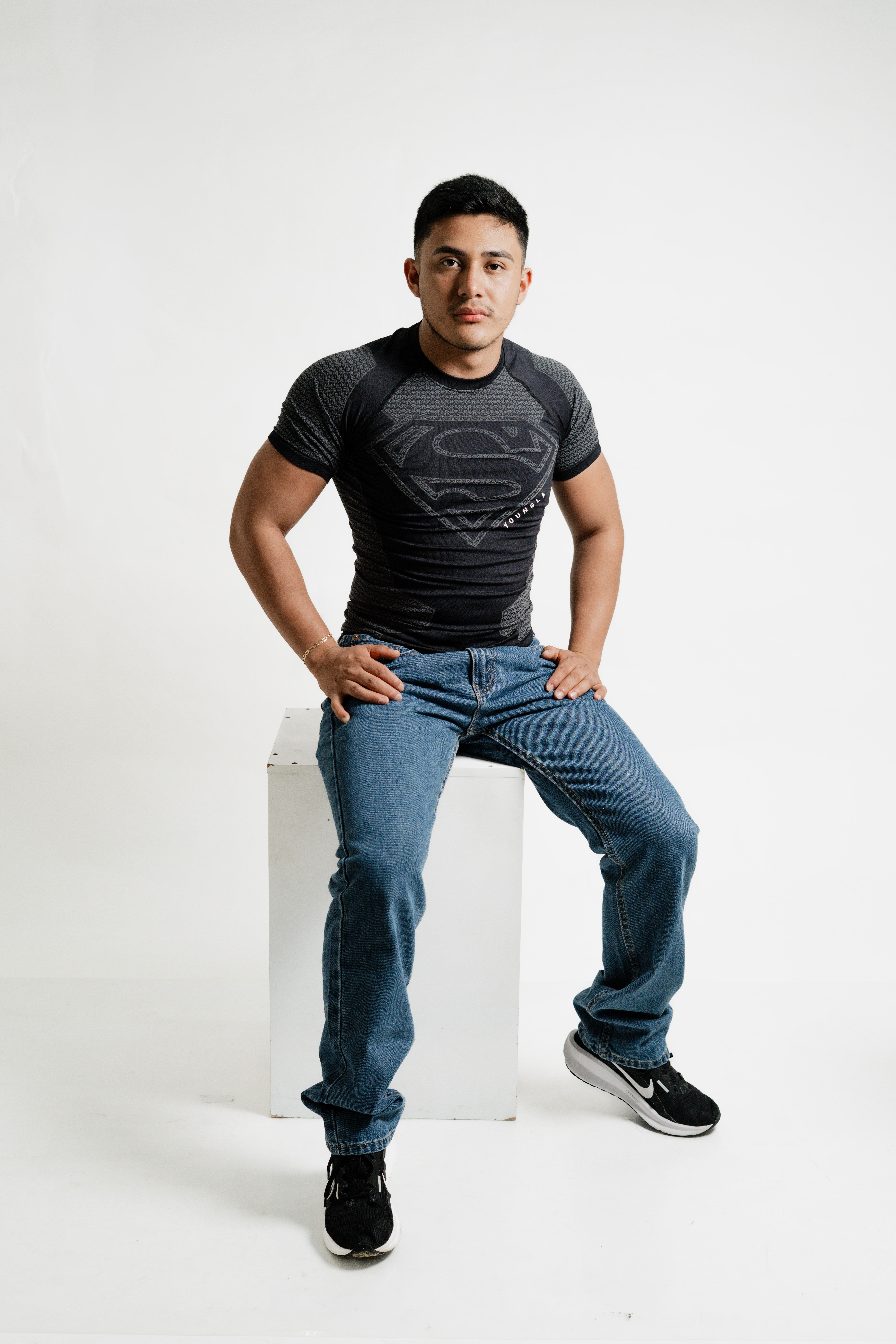 Young man in casual attire sitting on a stool against a white background.