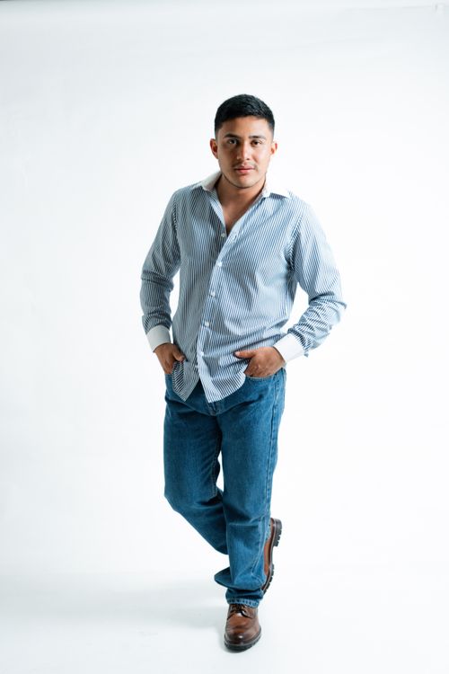 Free Portrait of a young man in a relaxed pose wearing a striped shirt and jeans in a studio. Stock Photo