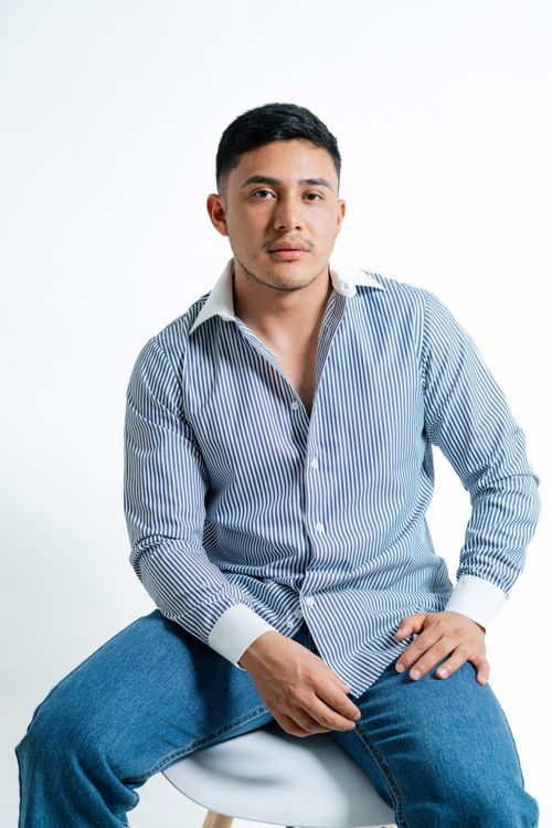 Free A young man in a striped shirt sits on a stool against a plain background. Stock Photo