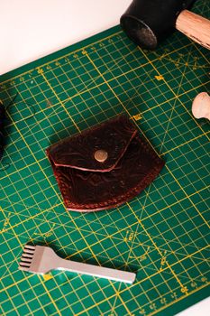 Top view of a handcrafted leather wallet on a green cutting mat with crafting tools.