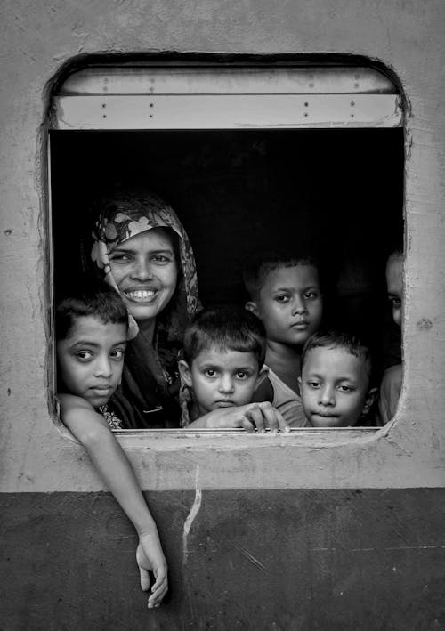 Black and white group of ethnic boys and girl riding on train and looking out open window