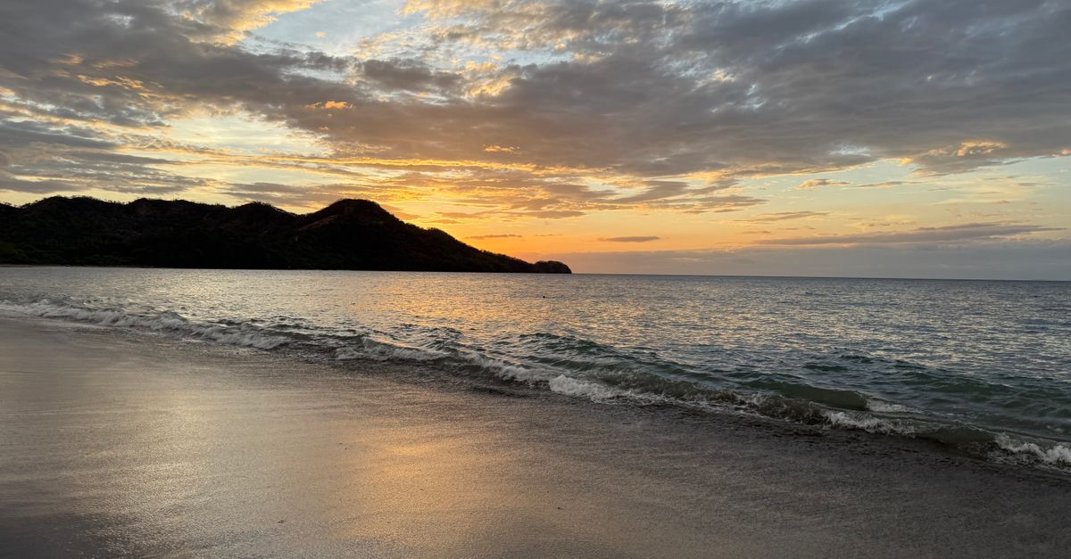Serene sunset over a tranquil Costa Rican beach with vibrant skies and gentle waves.