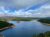 A tranquil view of a lake surrounded by lush forests and hills in Pampilhosa da Serra, Portugal.