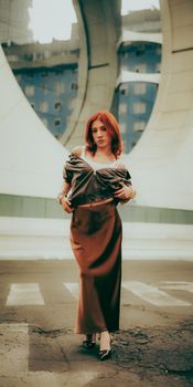 Stylish woman with red hair poses confidently in modern city architecture.