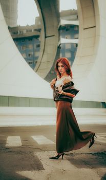 Stylish woman with red hair posing confidently in front of modern architecture.