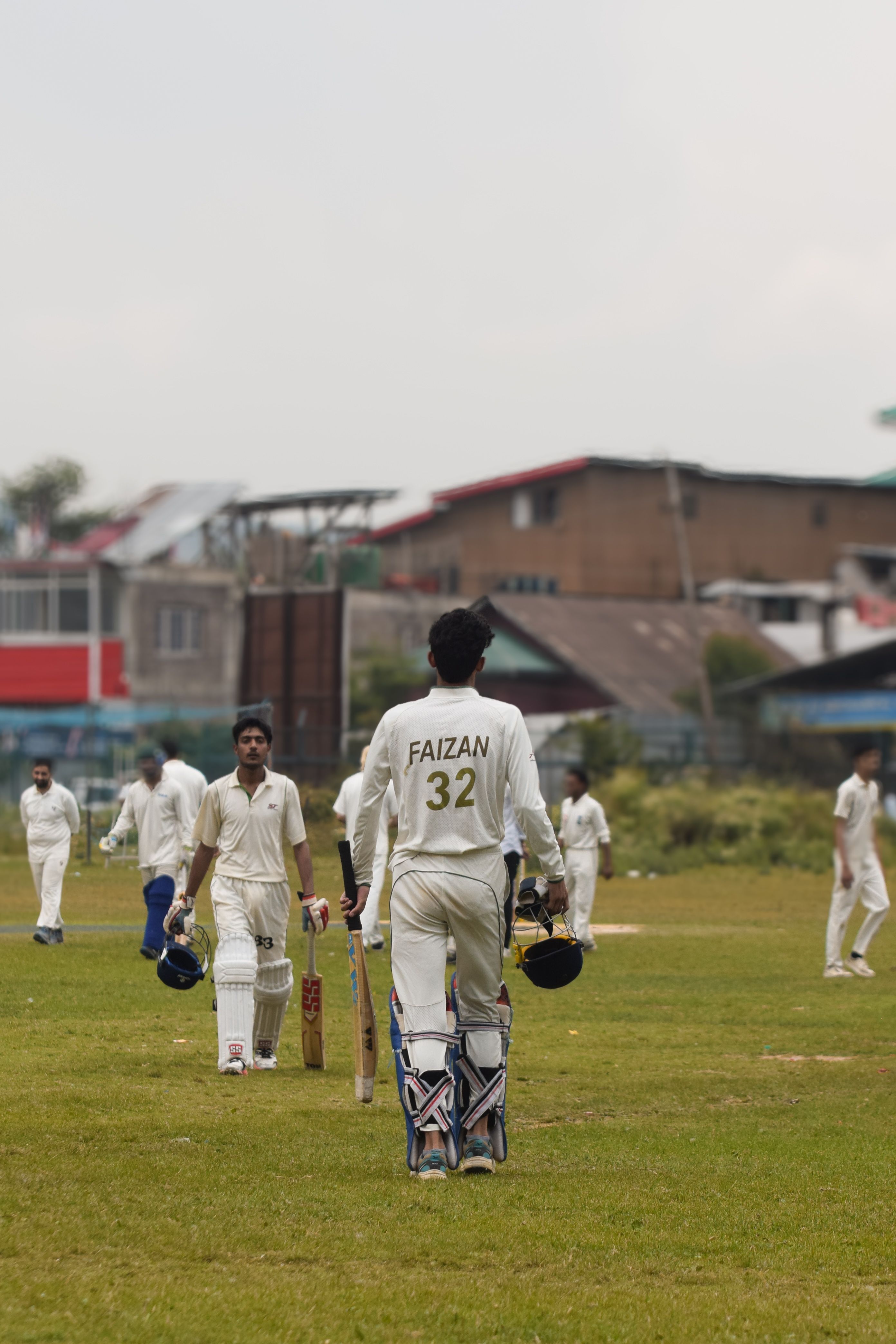 Cricket players in white uniforms play a match on a green field, showcasing teamwork and sportsmanship.