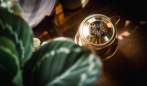 Free Top view of a brass tea kettle with a floral design surrounded by green foliage. Stock Photo