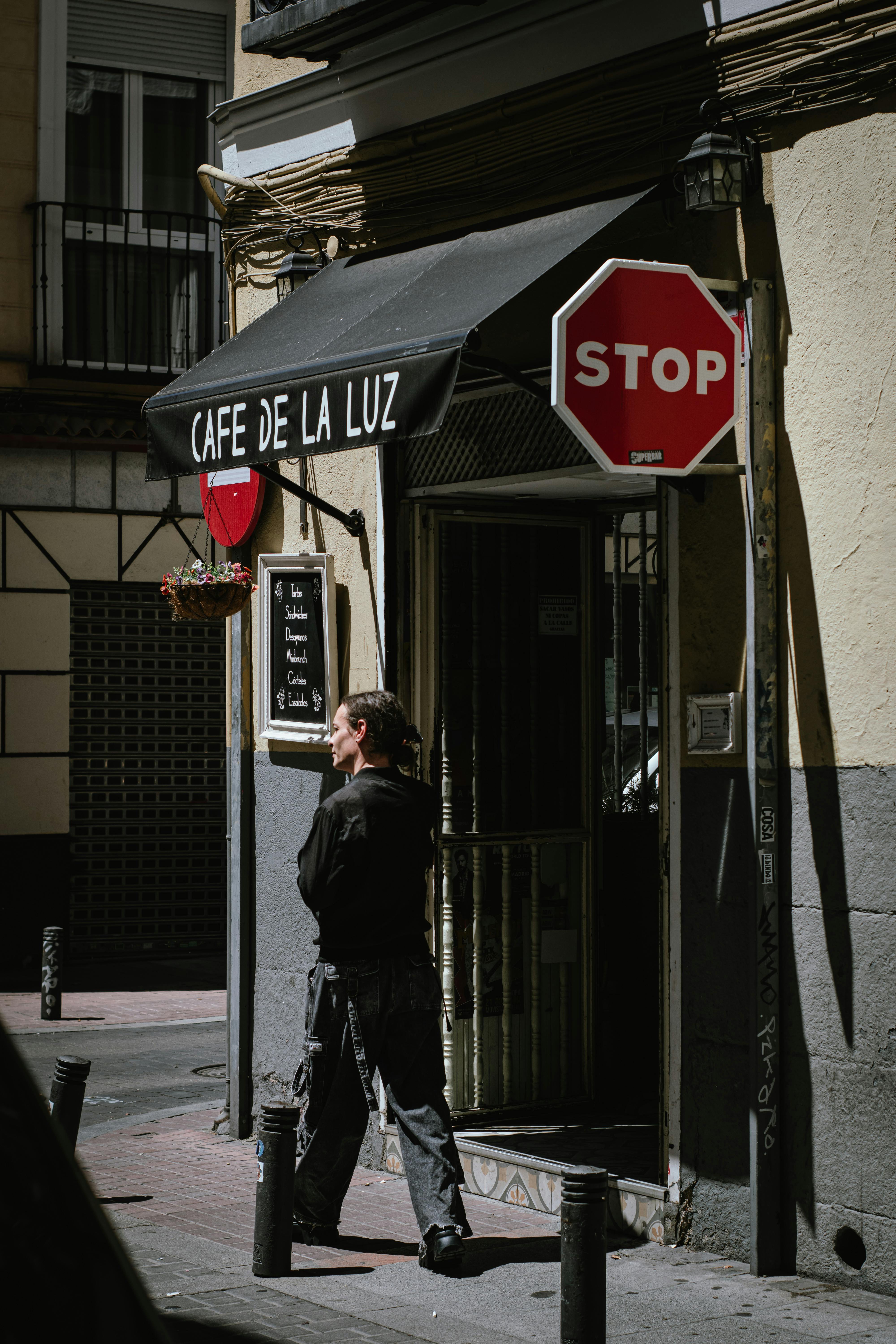 A man walks past Cafe de la Luz in Madrid with a stop sign nearby, captured in bright sunlight.