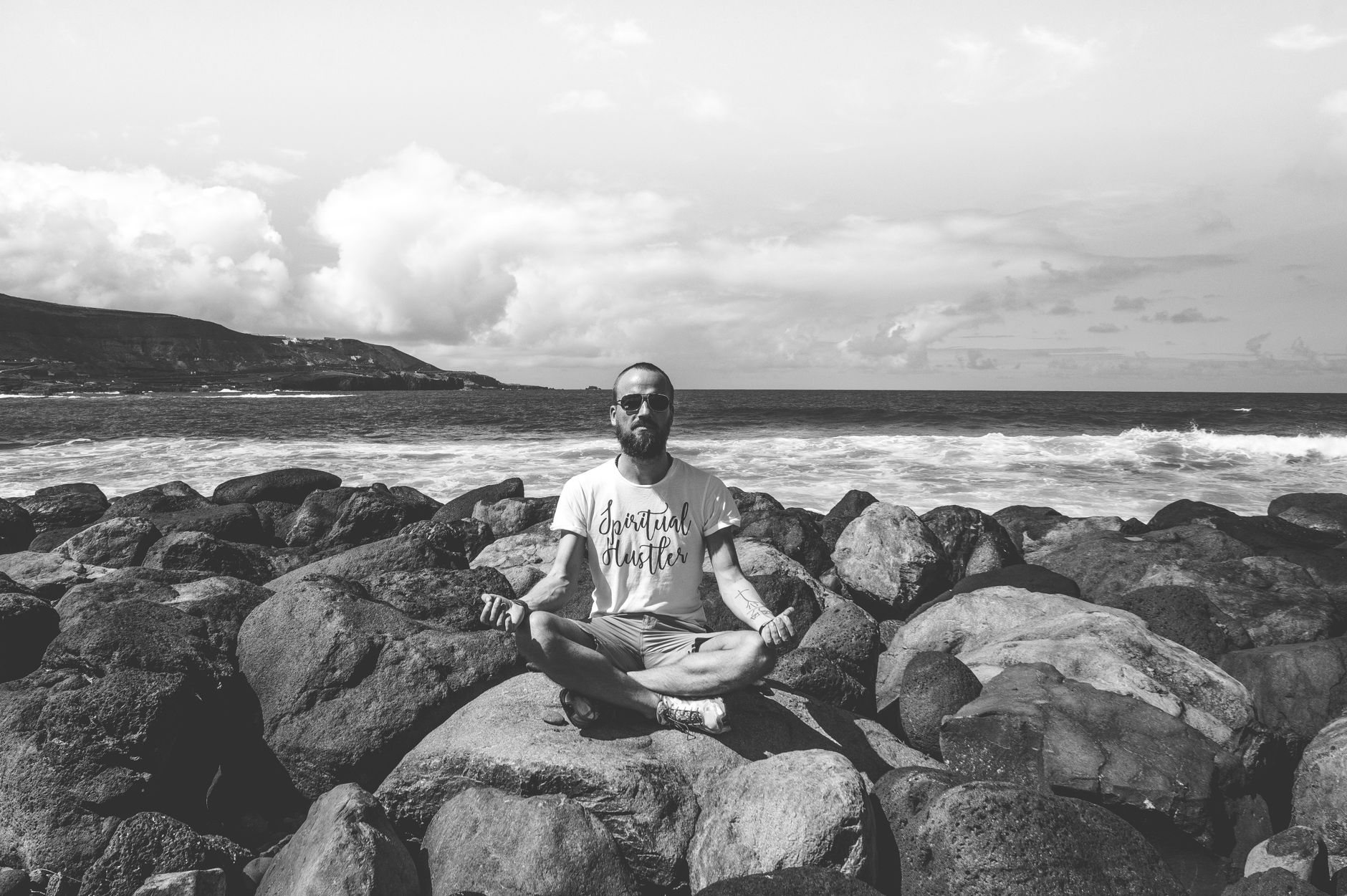Man in yoga pose meditating on a rocky shoreline, captured in black and white.