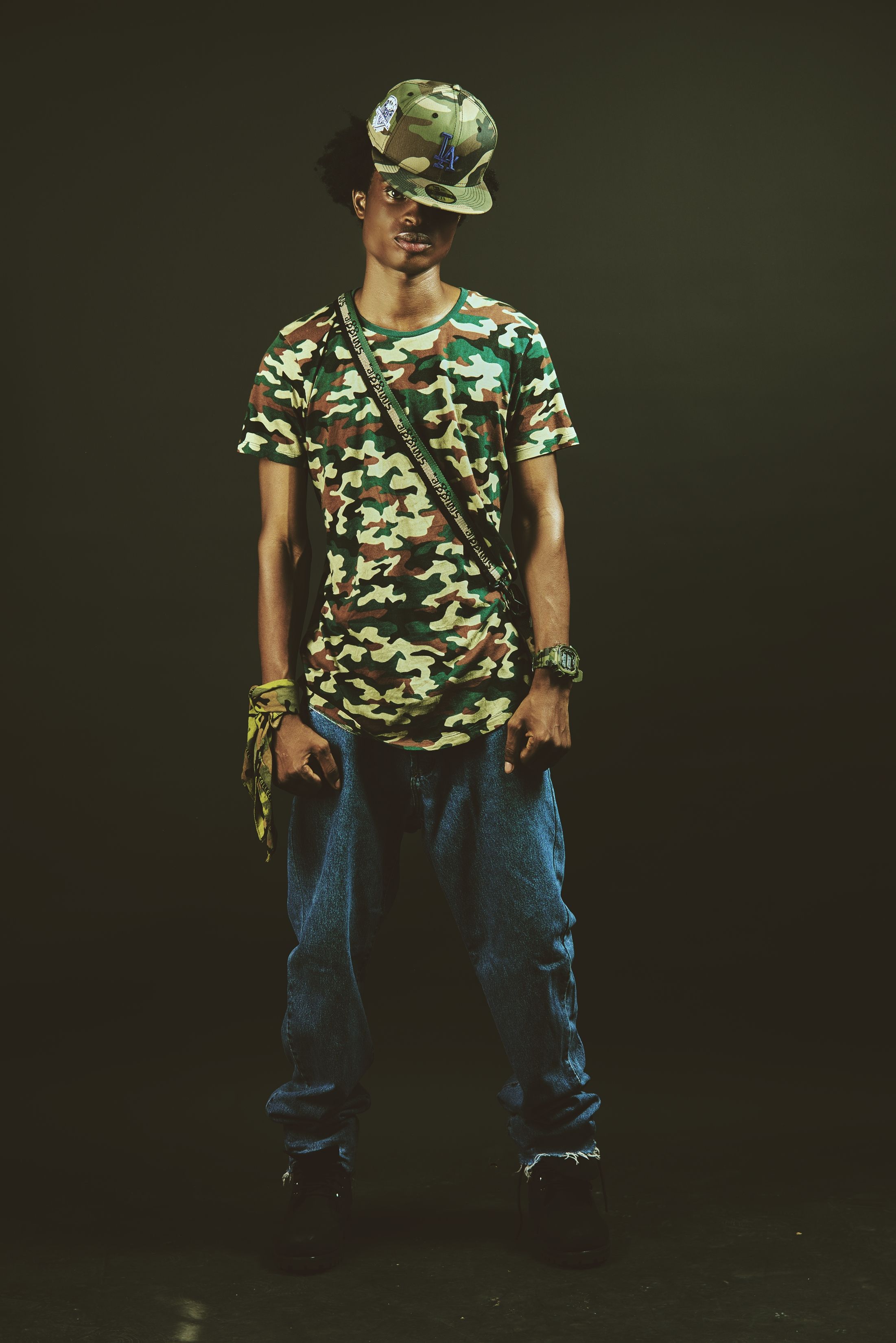 Portrait of a young man wearing a camouflage t-shirt and cap, standing confidently.