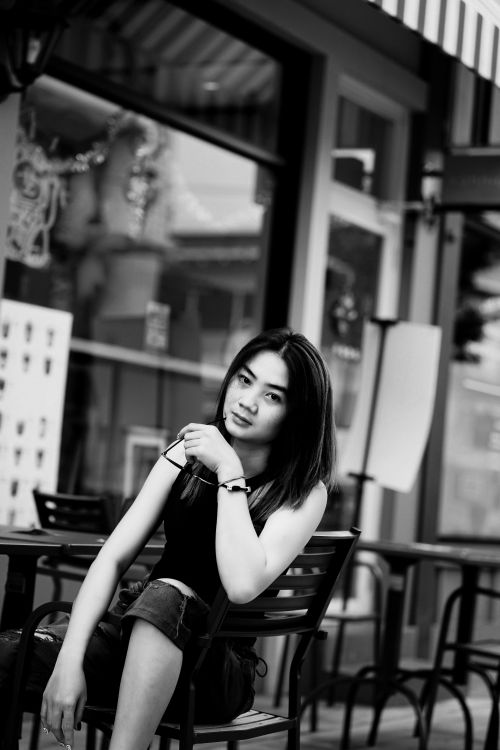 Free Black and white photo of a woman seated at an outdoor café with a contemplative look. Stock Photo