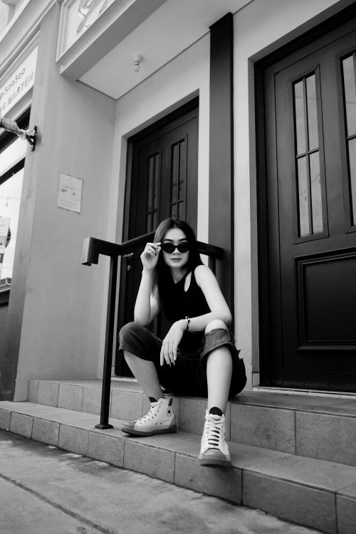 Free Monochrome portrait of a fashionable woman in casual attire sitting on outdoor steps. Stock Photo