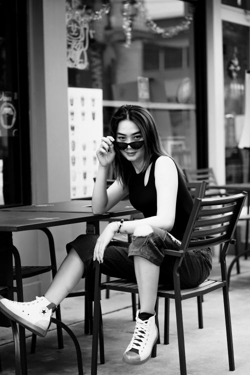 Free Casual portrait of a woman in sunglasses sitting at a cafe in black and white. Stock Photo