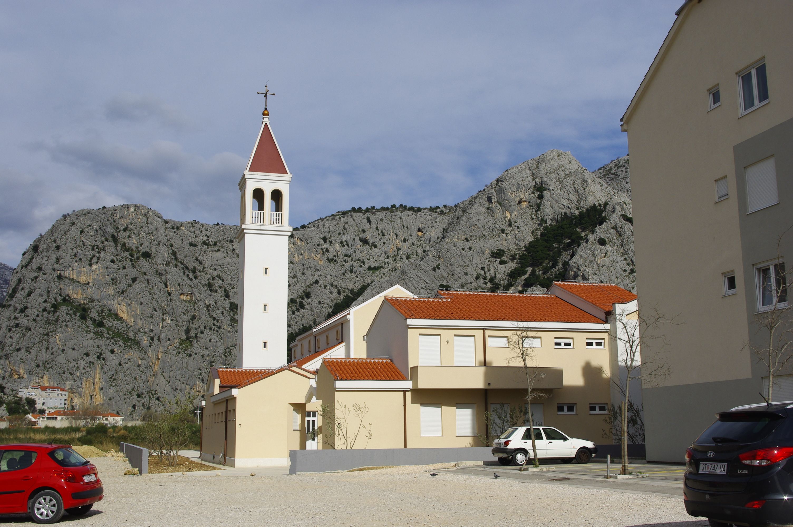 Serene view of a church tower in Omiš, Croatia, framed by rugged mountains.