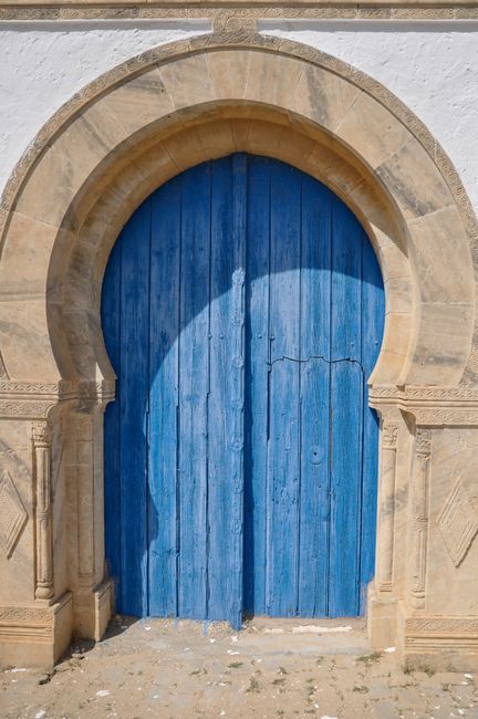 Historic Tunisian stone arch with blue wooden door in Tunis, showcasing traditional architecture.