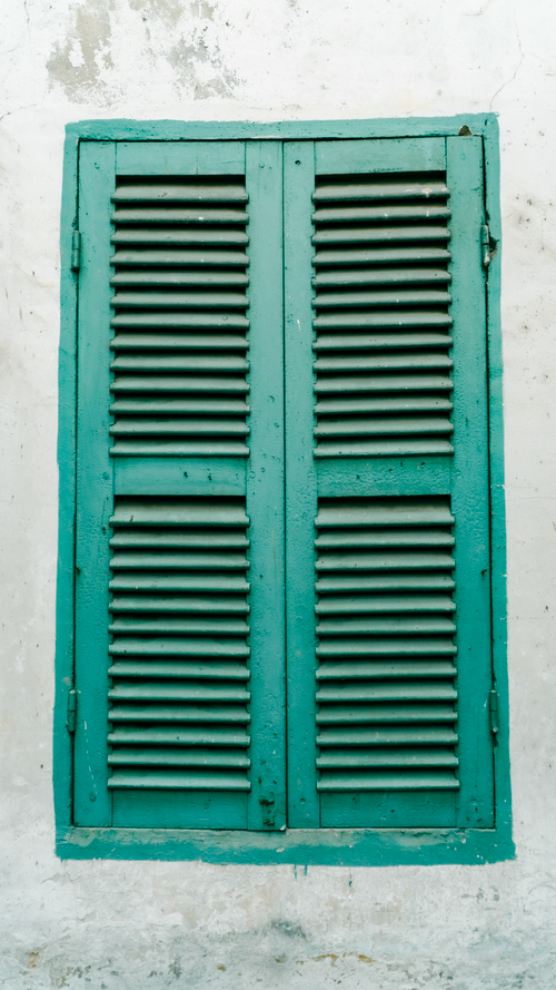 Free Photograph of a vintage green shuttered window set on a weathered white wall, exuding rustic charm. Stock Photo