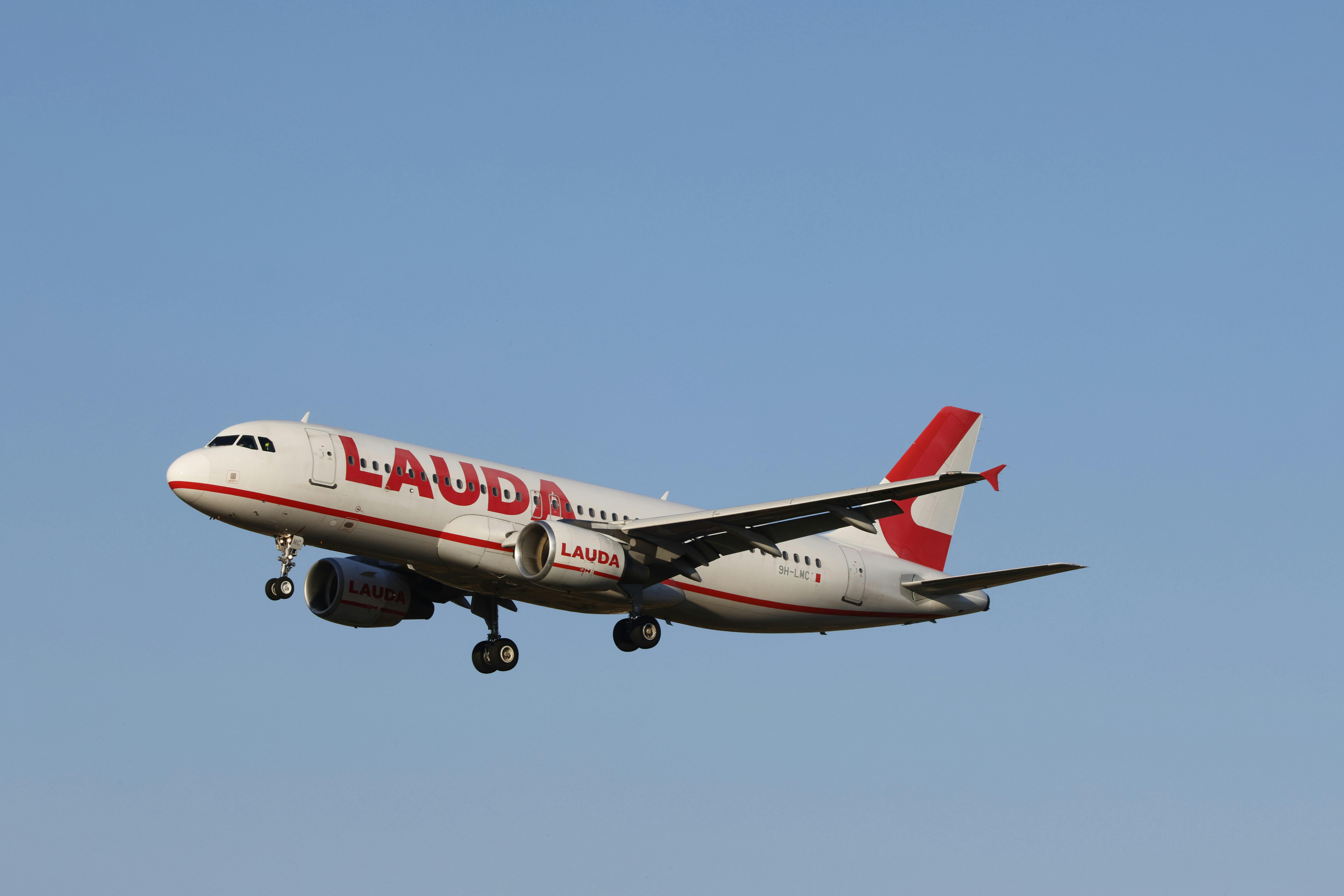 Side view of a Lauda airplane mid-flight against a clear blue sky, wings extended.