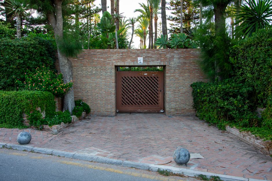 A rustic Mediterranean gate surrounded by lush greenery and brick architecture creates a serene outdoor scene.