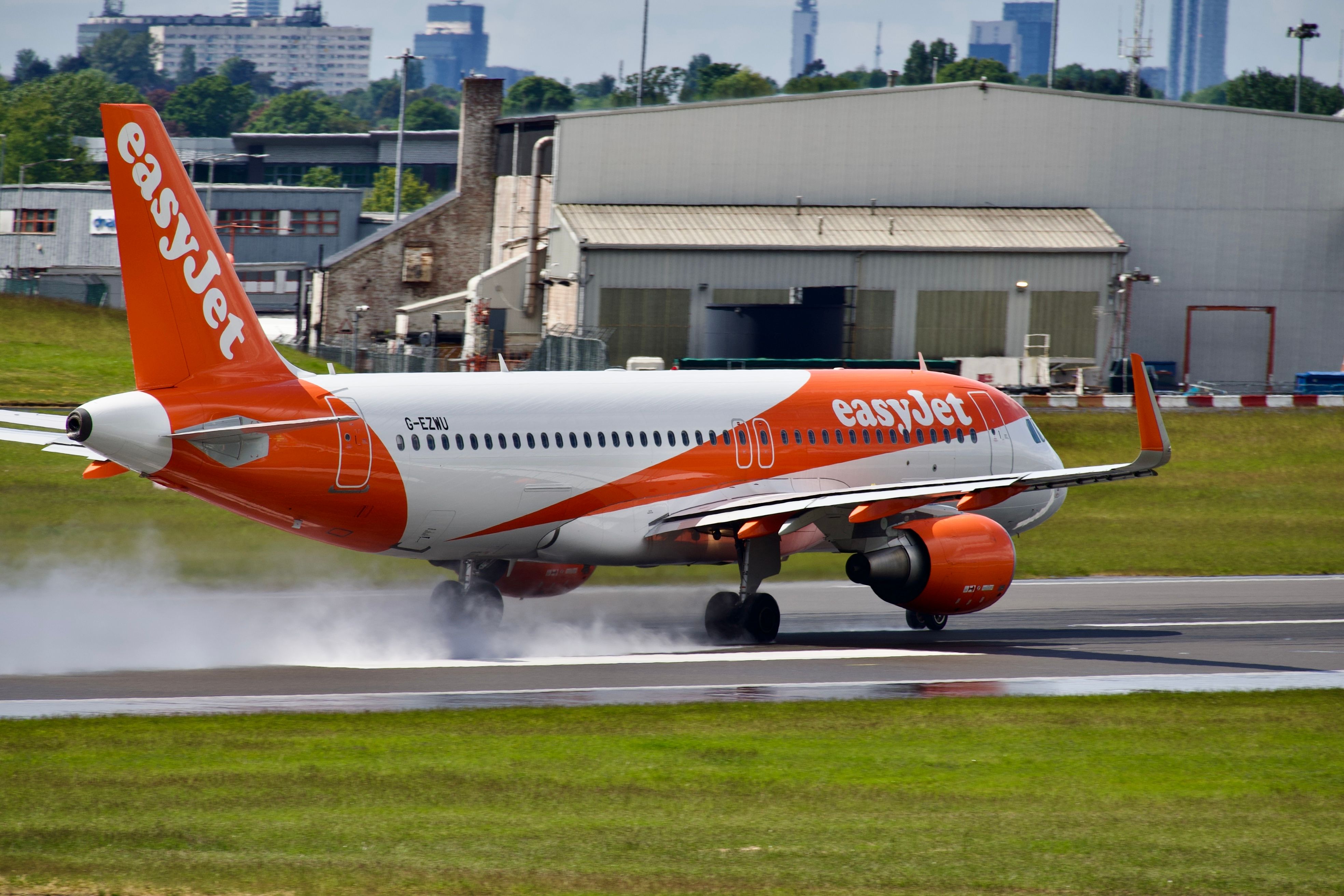 EasyJet airplane landing on a wet airport runway with water spray.