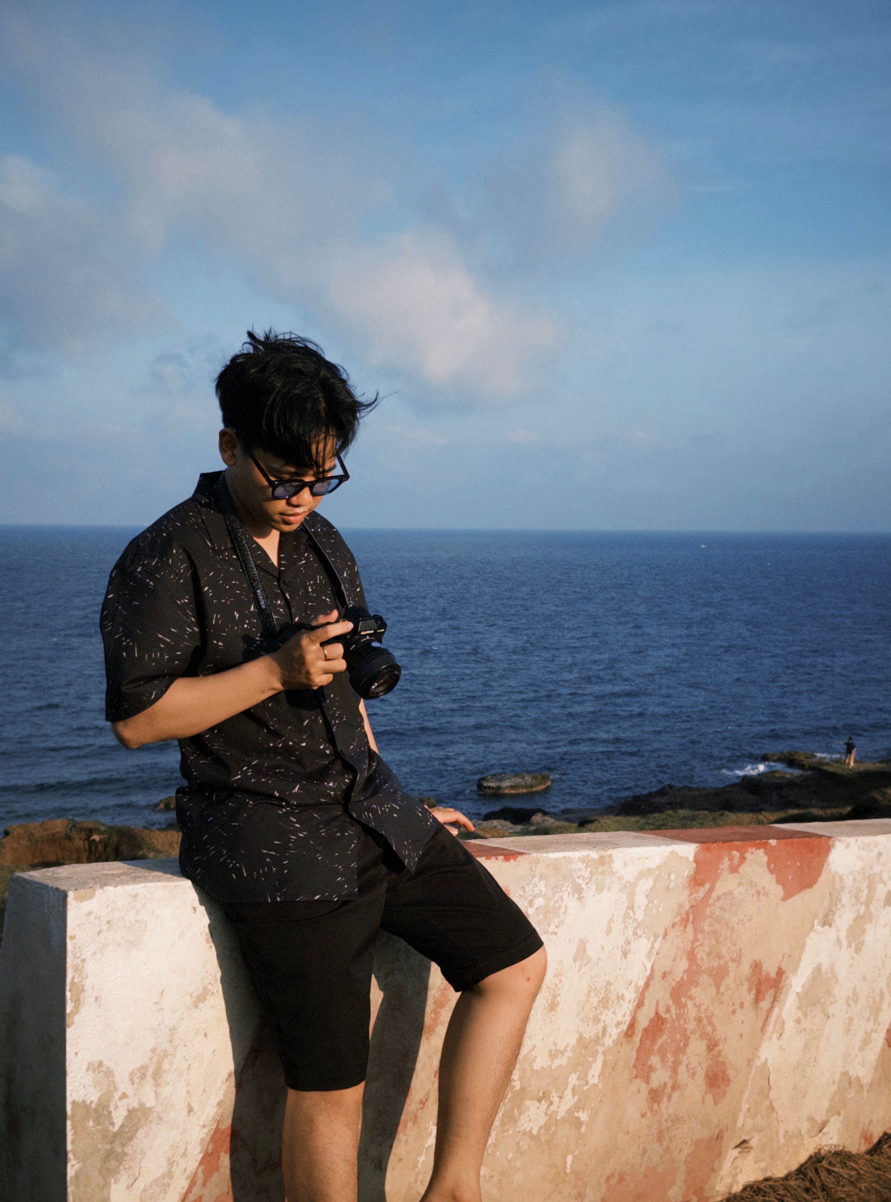 A young man with a camera enjoys a calm day by the sea, capturing the ocean's serene beauty.