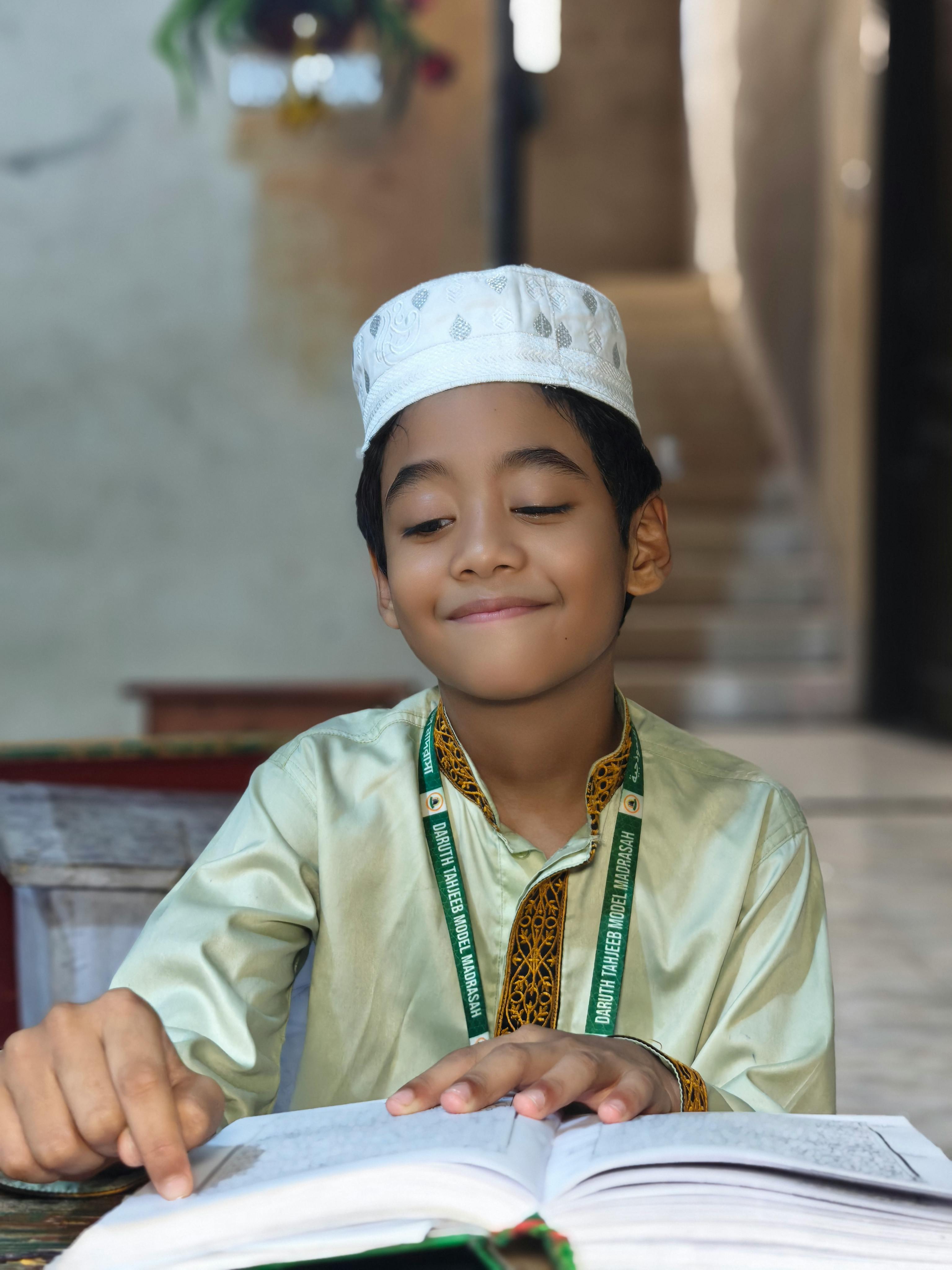 A focused young boy wearing traditional attire reads a book indoors, engaged in study.