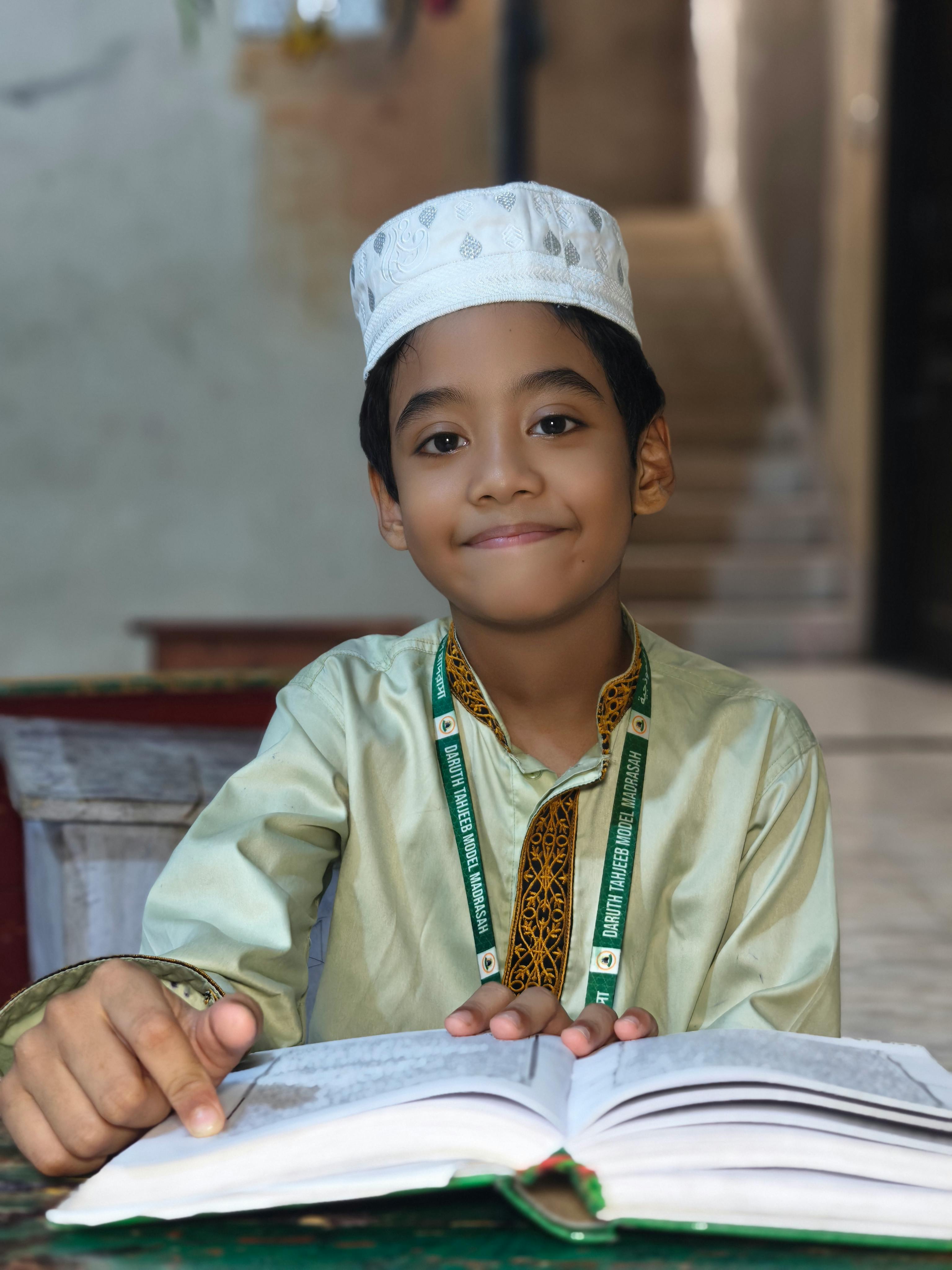 Portrait of a young boy in traditional attire reading Quran indoors, conveying education.