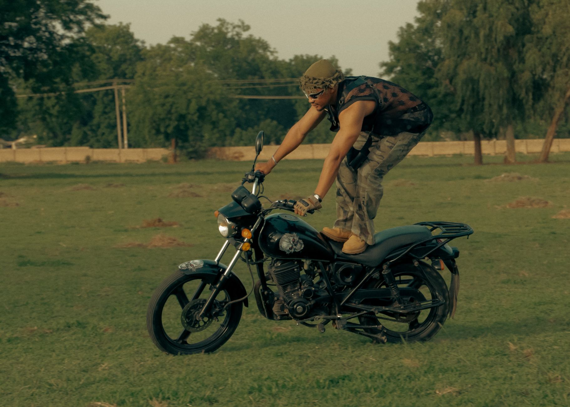 Adult male performing a daring motorcycle stunt in an open field during daytime.