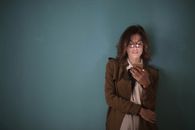 一位棕色头发、戴着眼镜的女士在室内茶色墙壁前使用智能手机