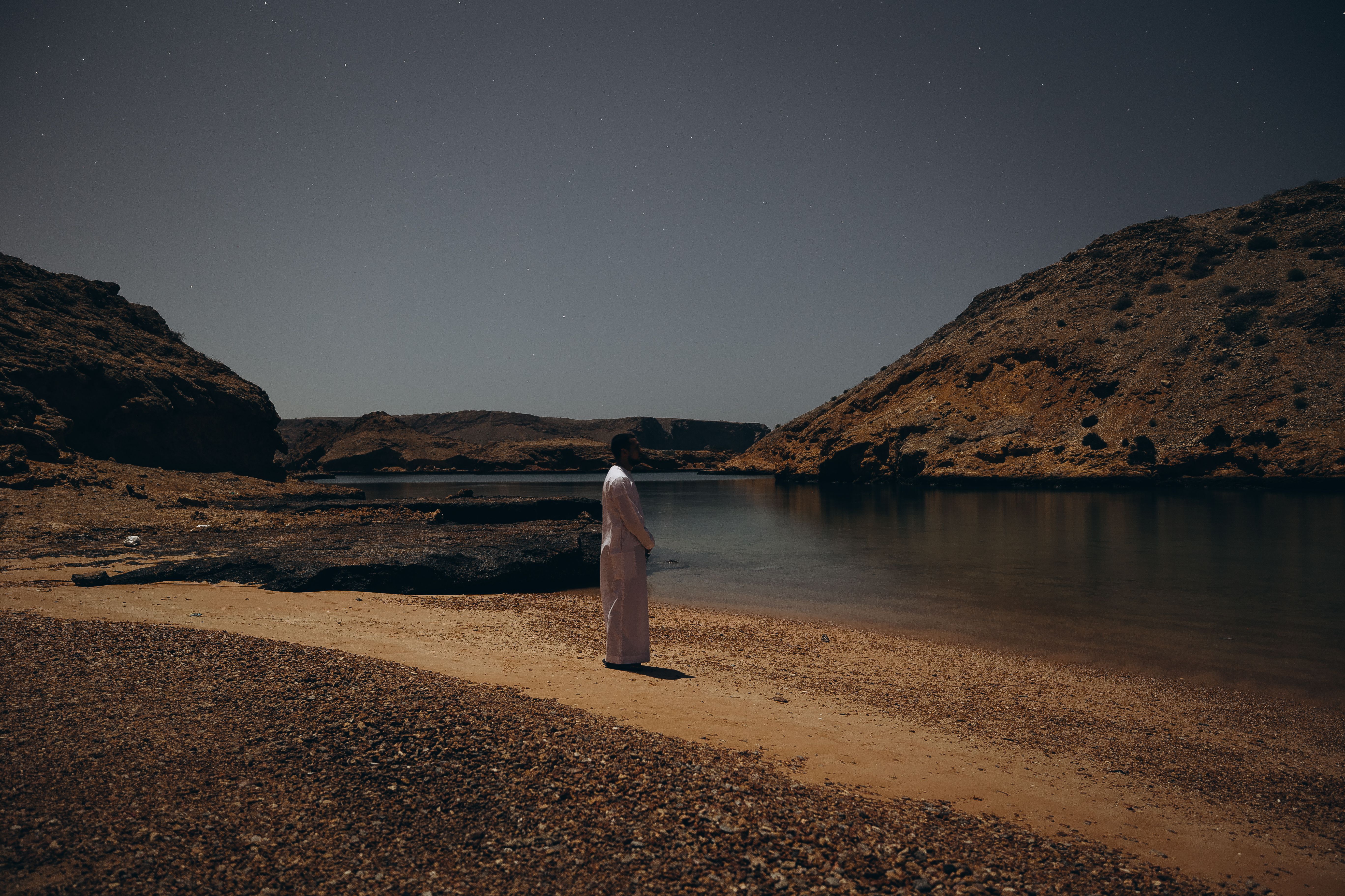 A serene evening view of a person standing by the shore in Muscat, Oman.