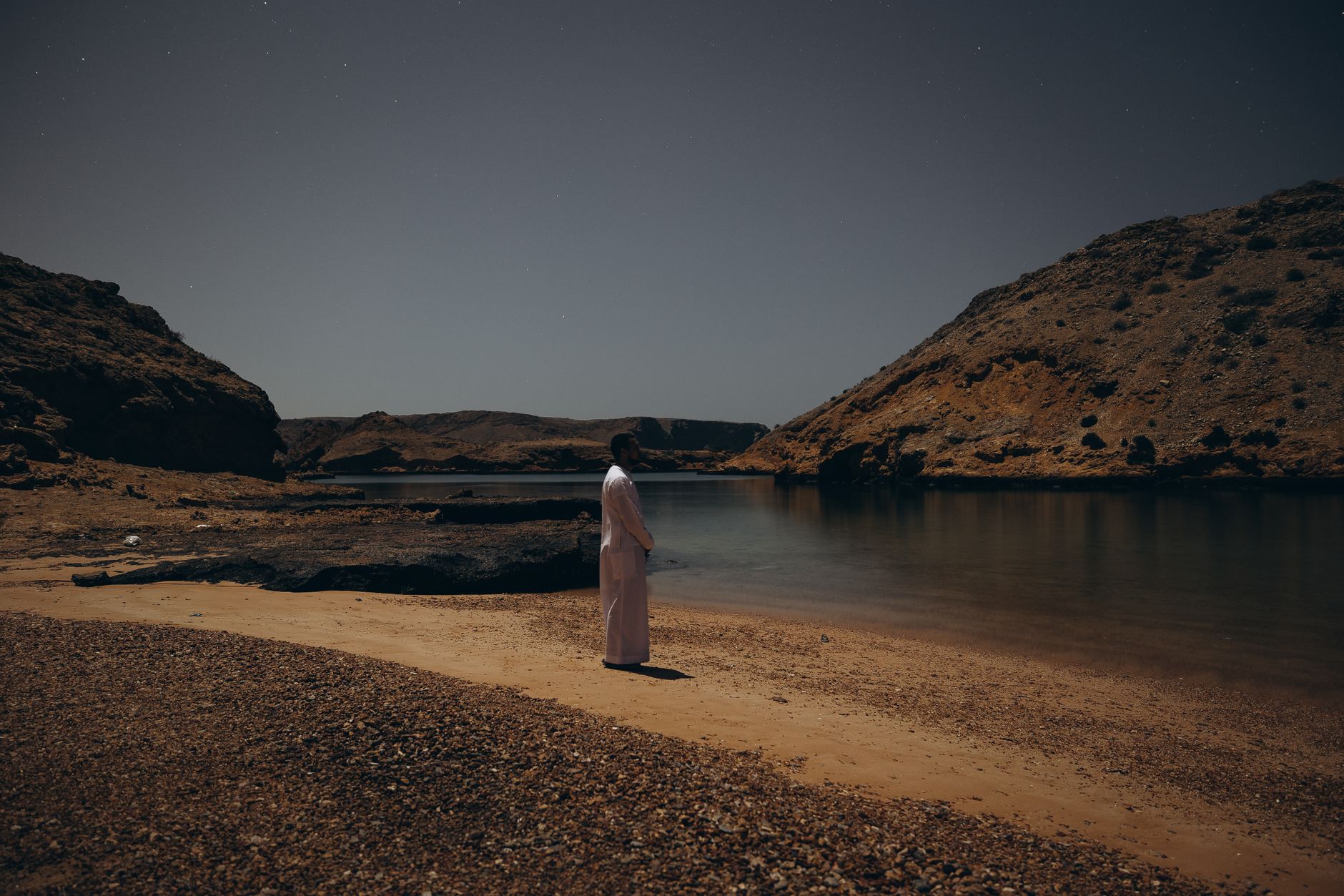 A serene evening view of a person standing by the shore in Muscat, Oman.