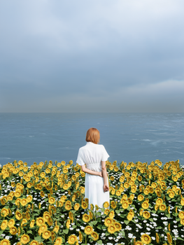 A woman stands in a sunflower field overlooking the sea on a cloudy day.