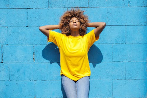 穿著黃色襯衫，倚著藍色磚牆的一位女士
