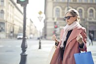 一位穿着粉红色外套、戴着墨镜、拿着袋子在城市街道上购物的优雅女子