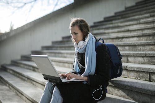 бесплатная Женщина, сидящая на бетонной лестнице с помощью ноутбука Стоковое фото
