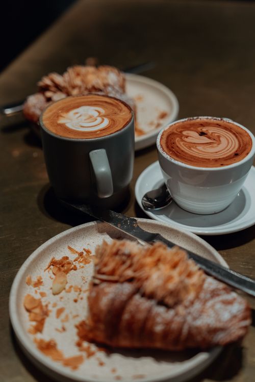 Free Stylish coffee and pastry setup in a cafe, showcasing cappuccinos with latte art and almond croissants. Stock Photo
