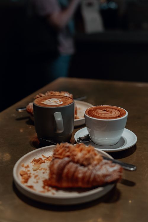 Free Warm café ambiance featuring croissants and lattes on a stylish table. Stock Photo