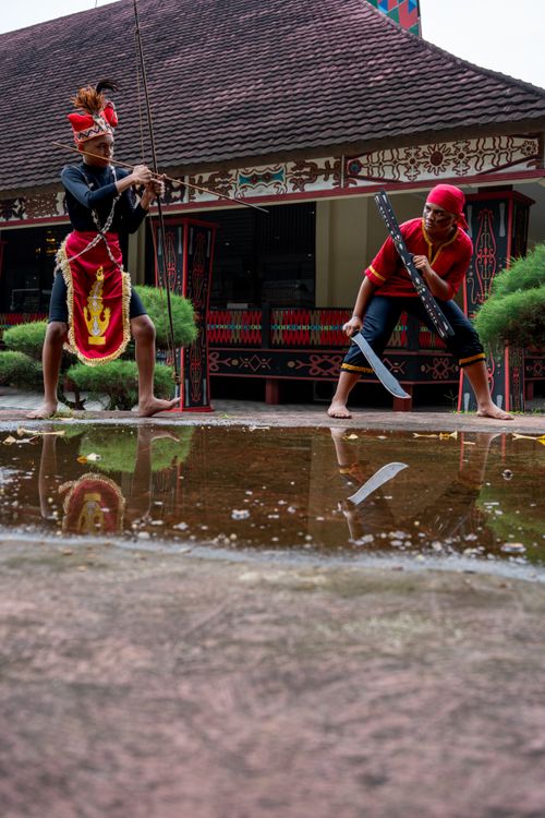 Free Two men in traditional attire engage in a cultural dance by a reflective puddle outdoors. Stock Photo