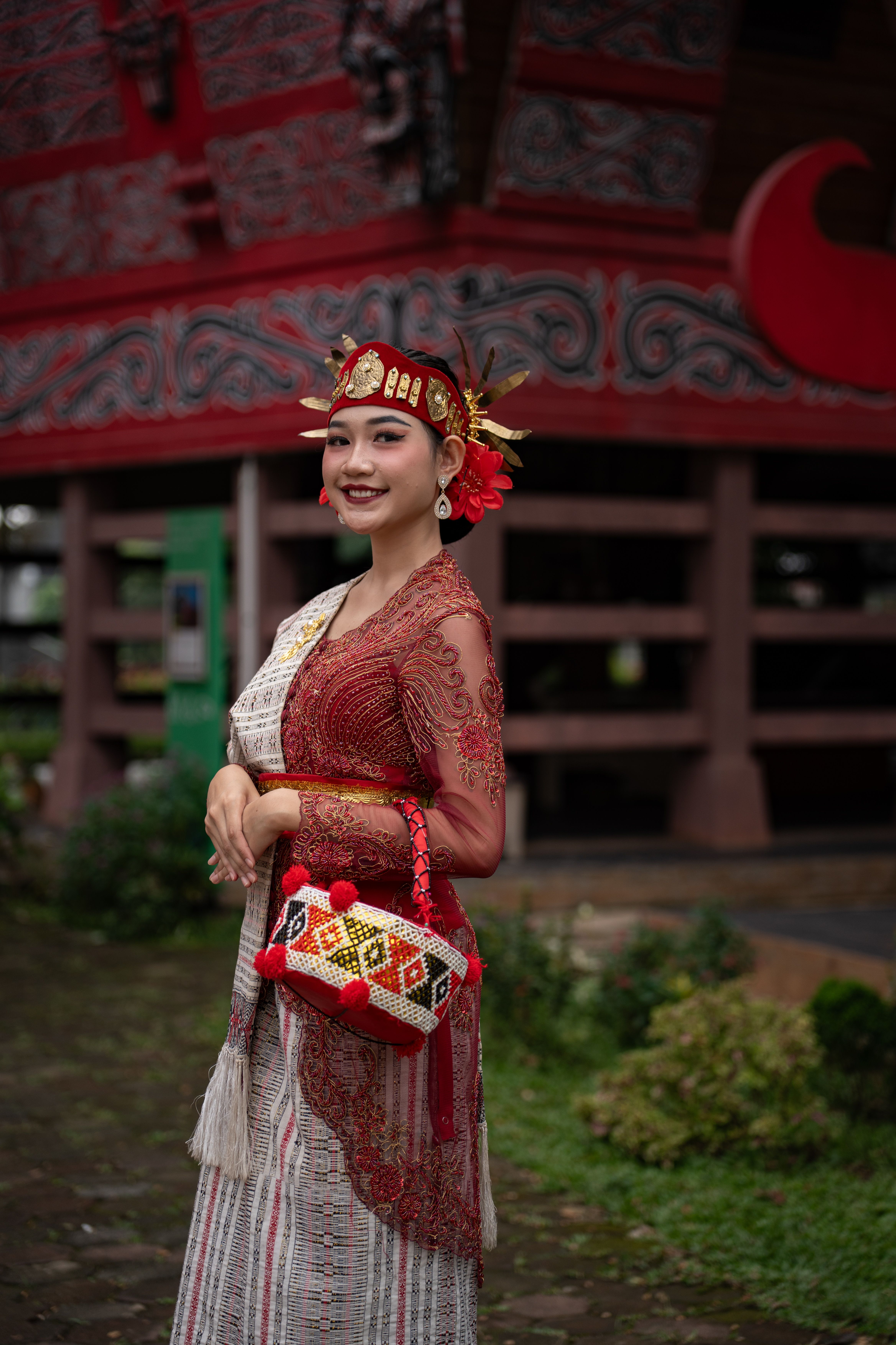Gratuit Femme en tenue traditionnelle rouge souriant à l'extérieur, près d'un bâtiment richement décoré. Photos