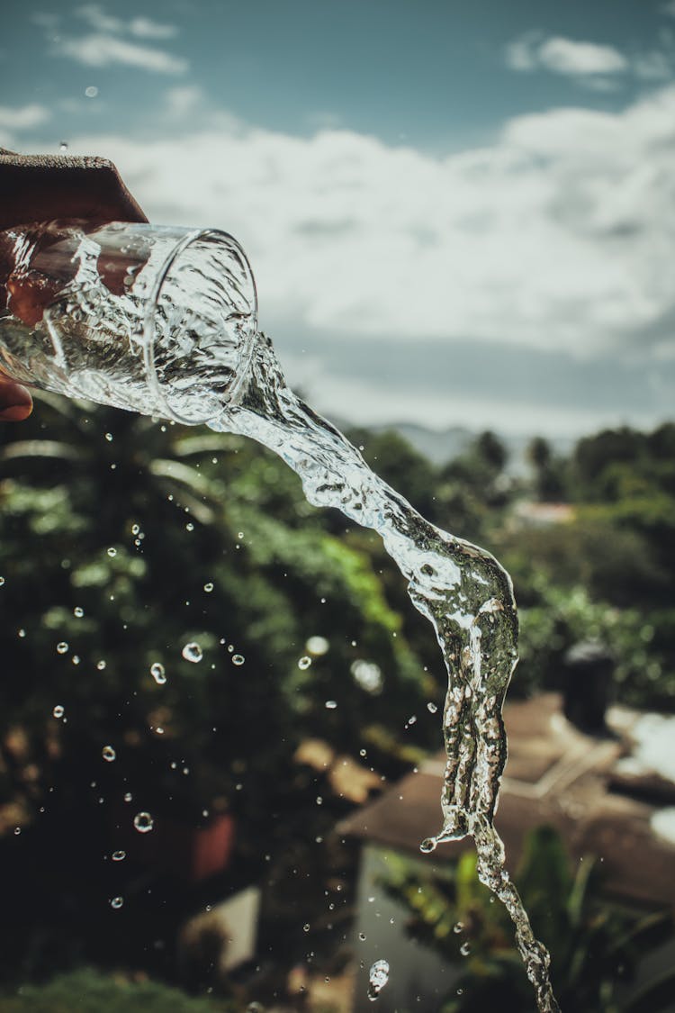 A Man Pouring A Glass Of Water Under Cloudy Sky