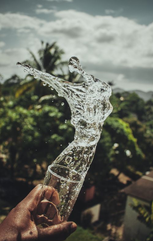Free A hand capturing a dramatic splash of water mid-air against a lush outdoor backdrop. Stock Photo