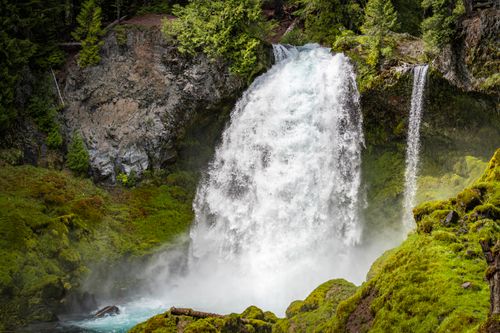 Free Scenic waterfall cascading over mossy rocks surrounded by lush forest in spring. Stock Photo