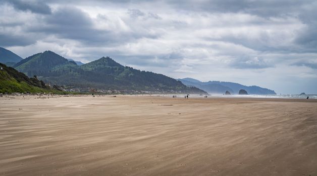 Expansive view of Cannon Beach, Oregon with Haystack Rock and overcast sky in the background.