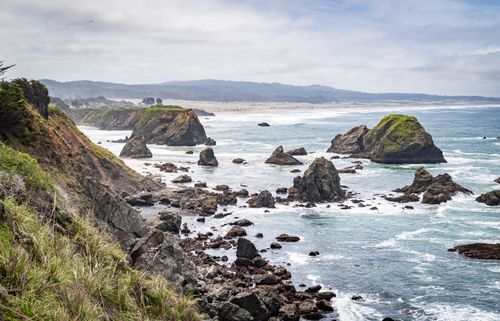 Free Stunning view of the Oregon coastline with rocky seascape and lush greenery under a cloudy sky. Stock Photo