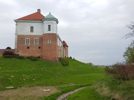 A picturesque historic castle on a lush green hill under a cloudy sky, showcasing medieval architecture.