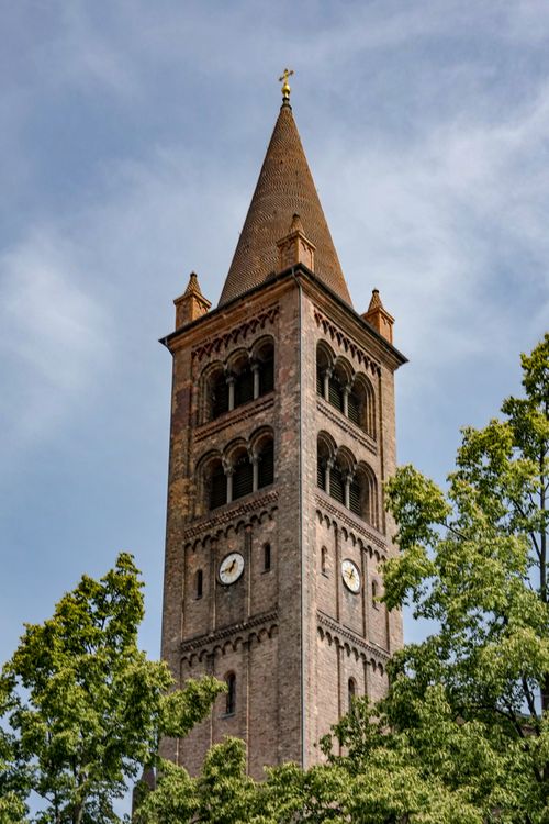 Free A historic brick bell tower in Potsdam, surrounded by lush trees under a clear sky. Stock Photo